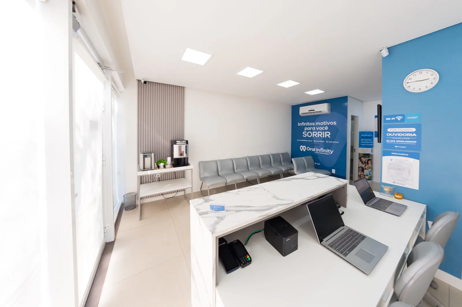 Recepção real da Oral Infinity — balcão de mármore, poltronas de espera e o mural da marca 'Infinitos motivos para você sorrir' na parede azul